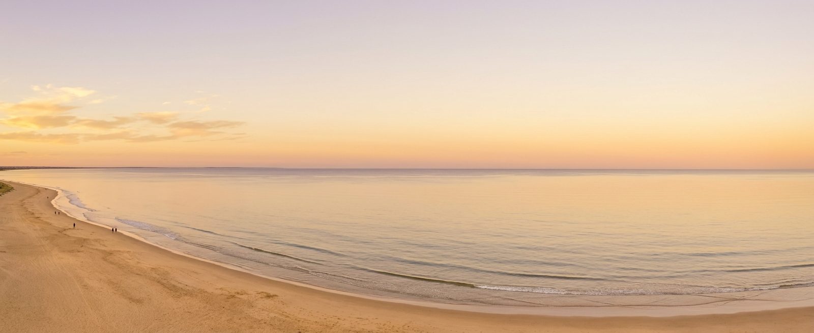 A calm, pastel-colored beach shoreline at sunrise